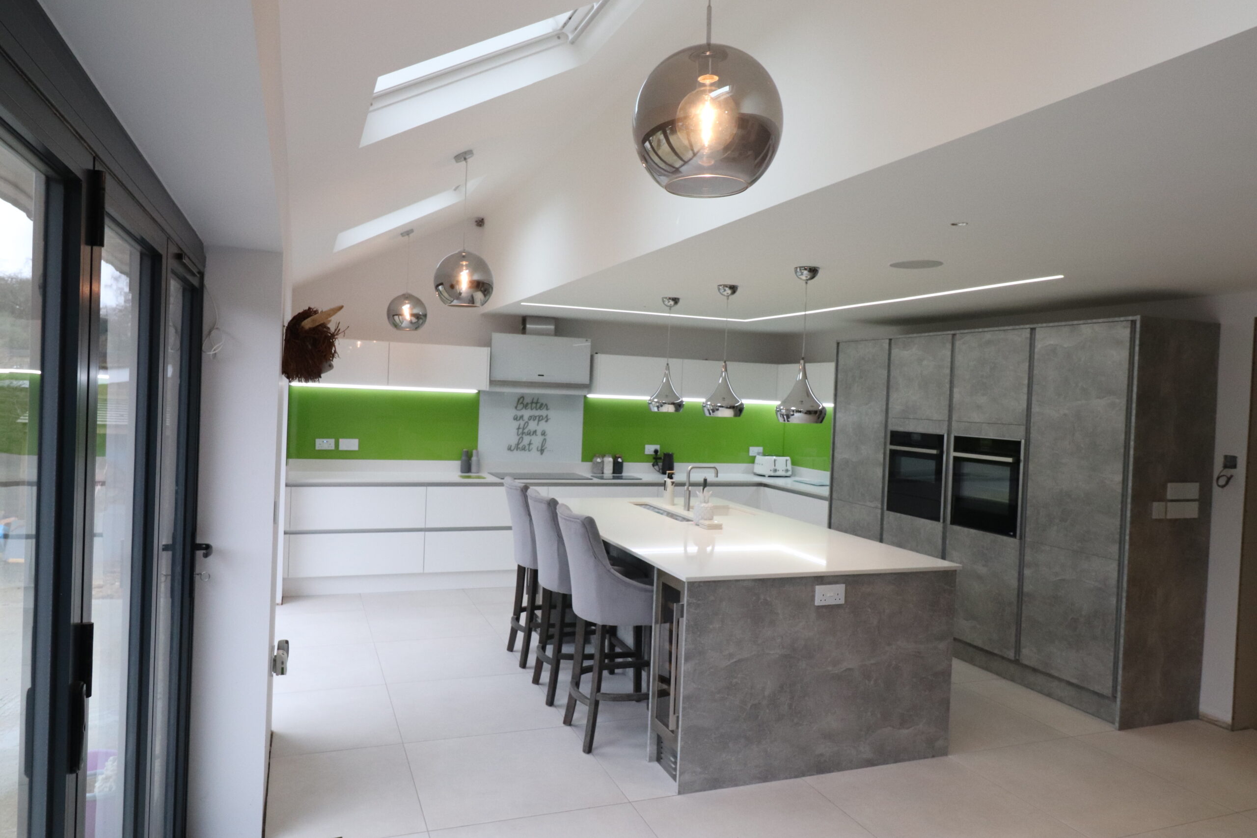 Modern family kitchen with large island seating, concrete-effect cabinetry and green splashback in Camberley