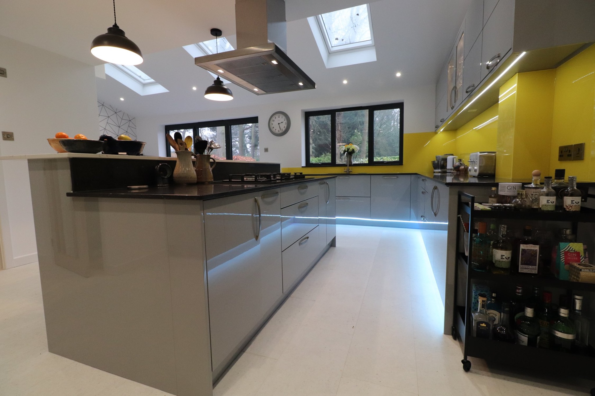Gloss grey handleless kitchen with black granite worktop, yellow glass splashback, LED plinth lighting and skylights — Inner Peace Interiors, Camberley
