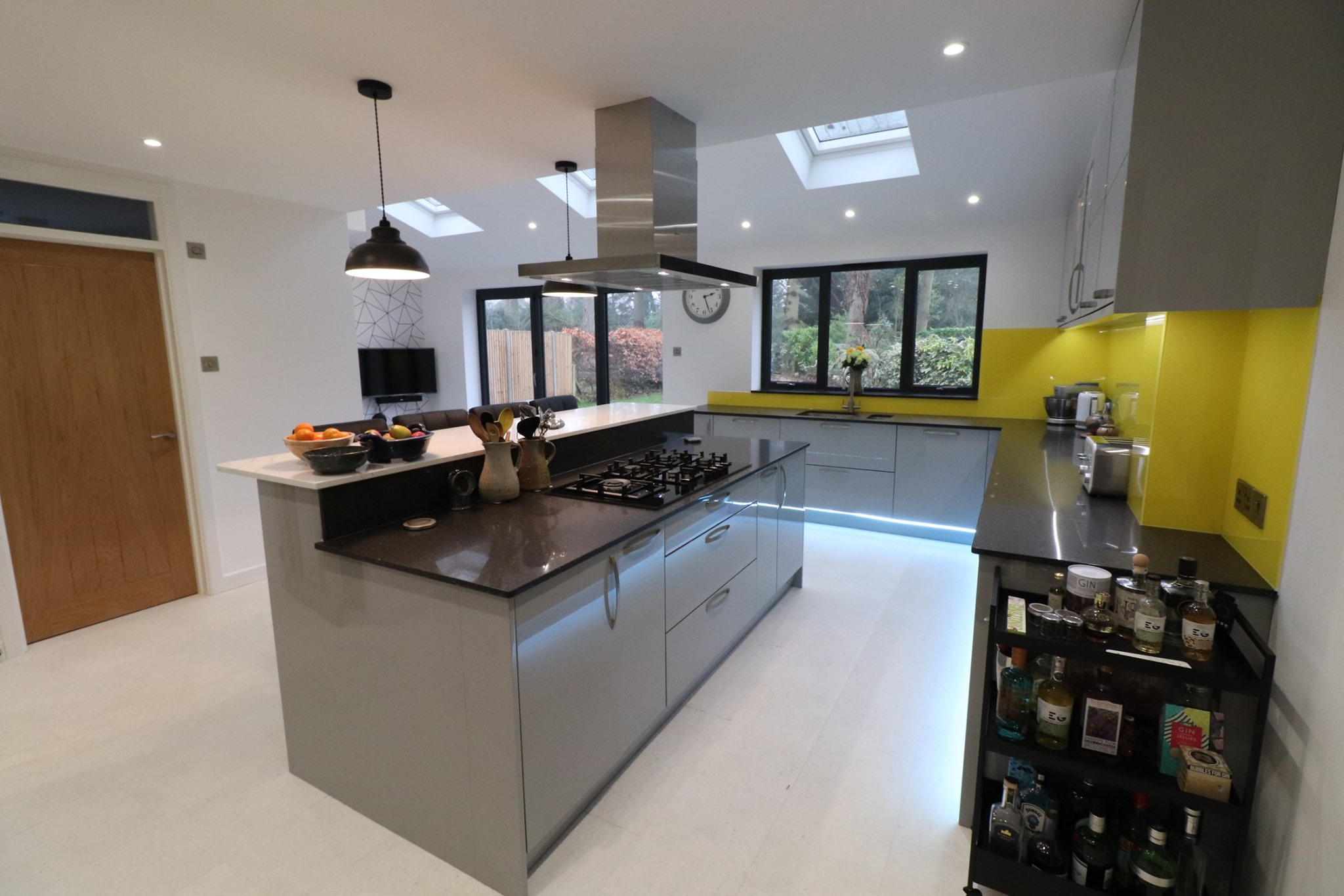 Gloss grey handleless kitchen with black granite island hob, yellow glass splashback and skylights in open-plan extension — Inner Peace Interiors, Camberley