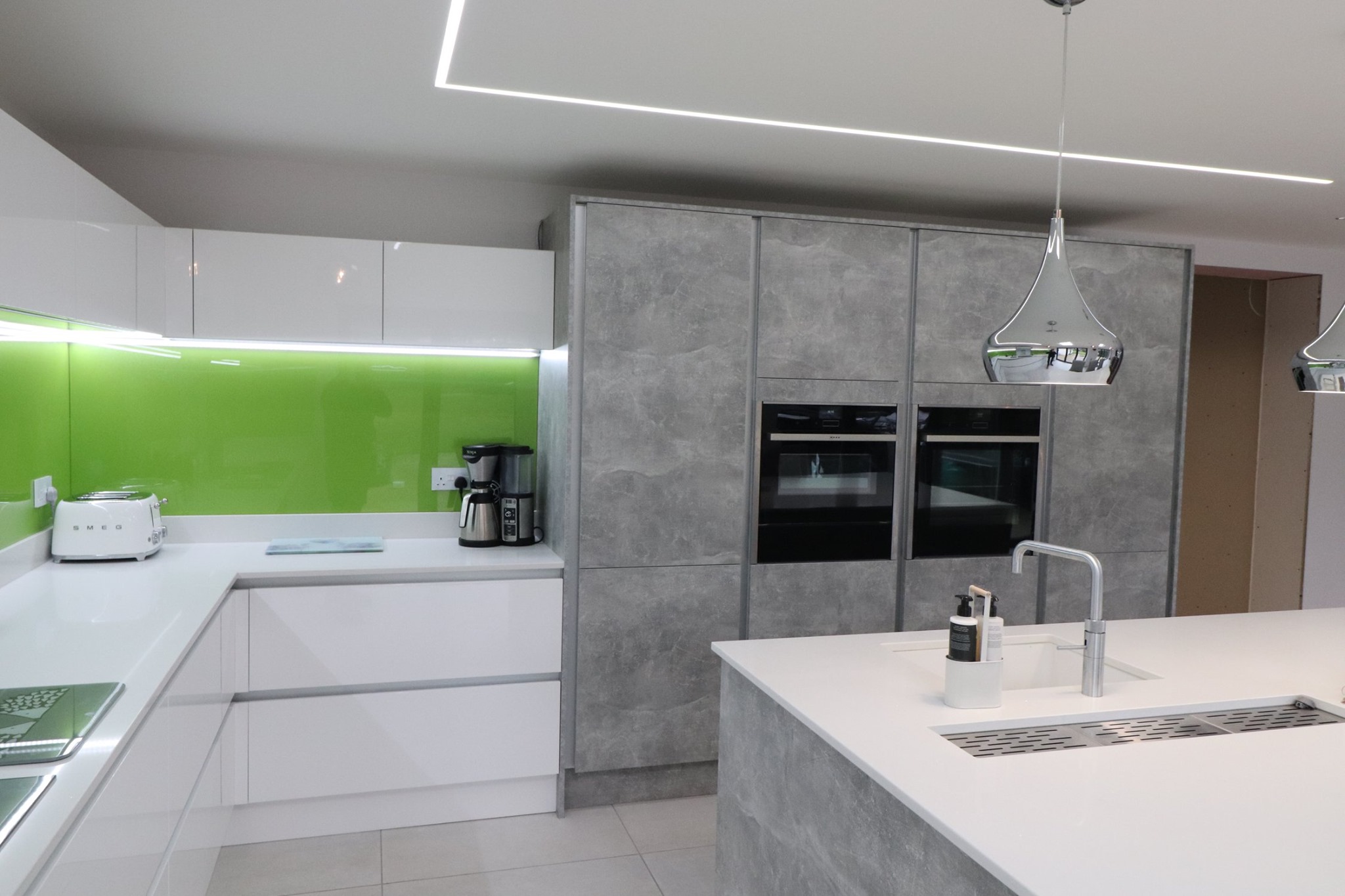 Modern handleless kitchen with white cabinetry, concrete-effect units and green glass splashback